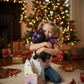 Child holding a plush toy in front of a decorated Christmas tree with presents - KWtoyszone | Proudly Canadian